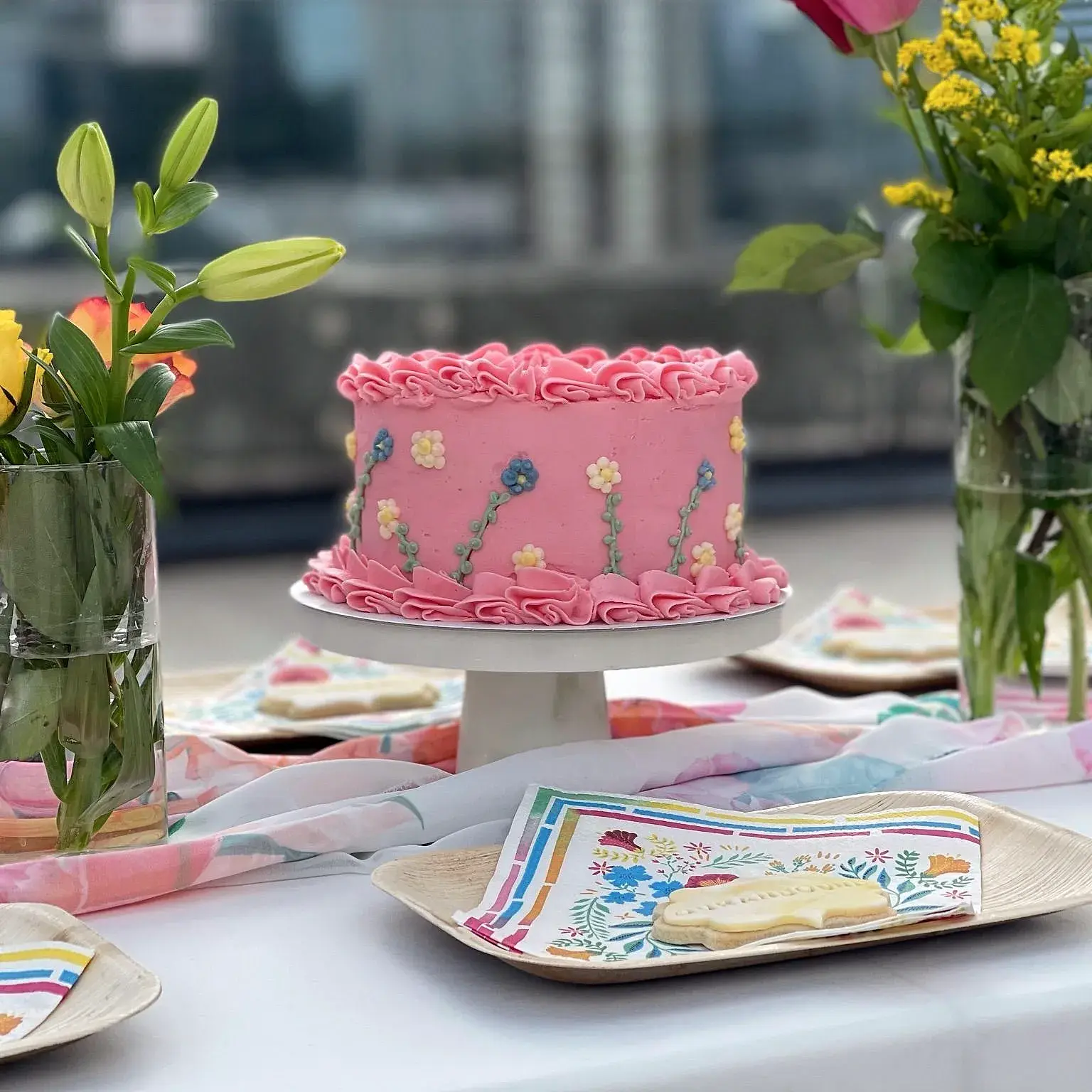 An ATTQ Sisters cake on a table with flowers, the city behind it